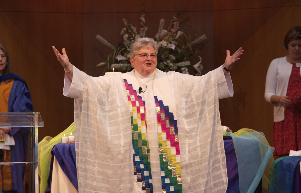 Rev. H. Sharon Howell in her religious robes and arms raised as she preaches