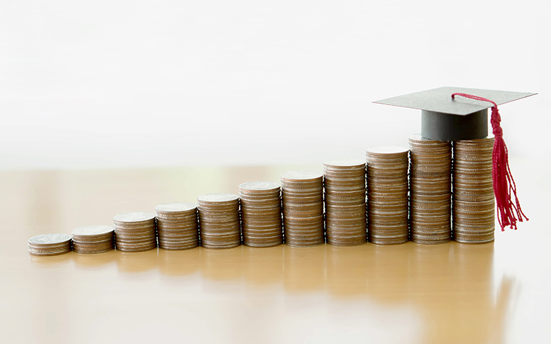 Several stacks of coins with a graduation cap represents the rising cost of education