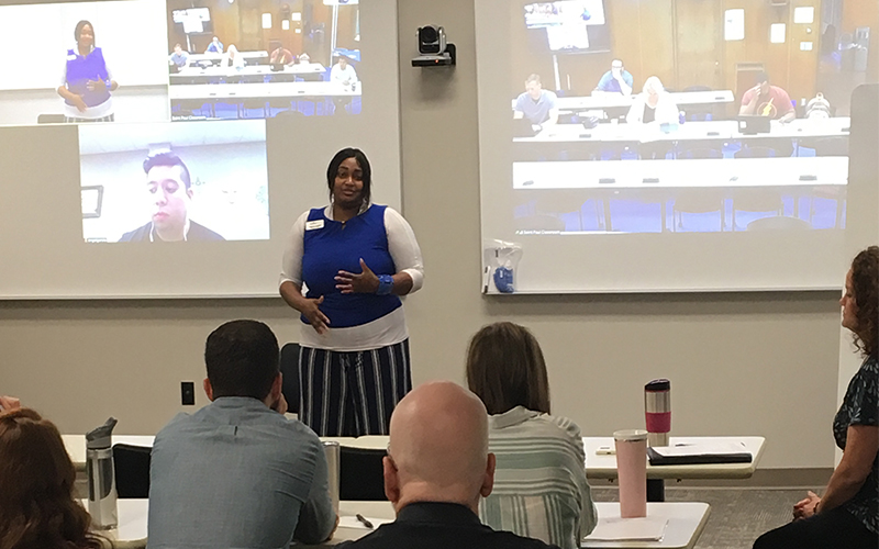 an instructor speaks to a group of students in the classroom and over video call